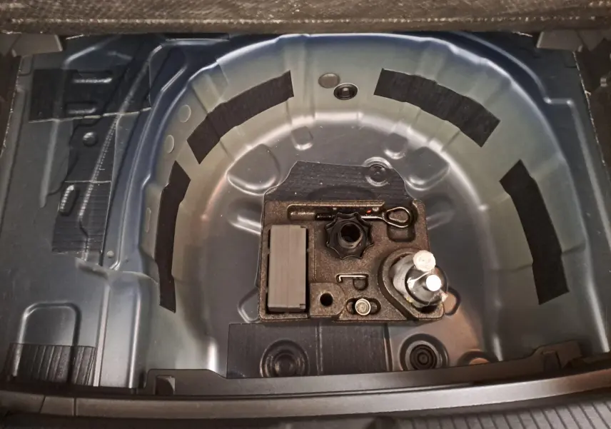Vue en plongée sur le coffre ouvert d'une Volkswagen Polo bleu récif, montrant le rangement pour roue de secours et outils.