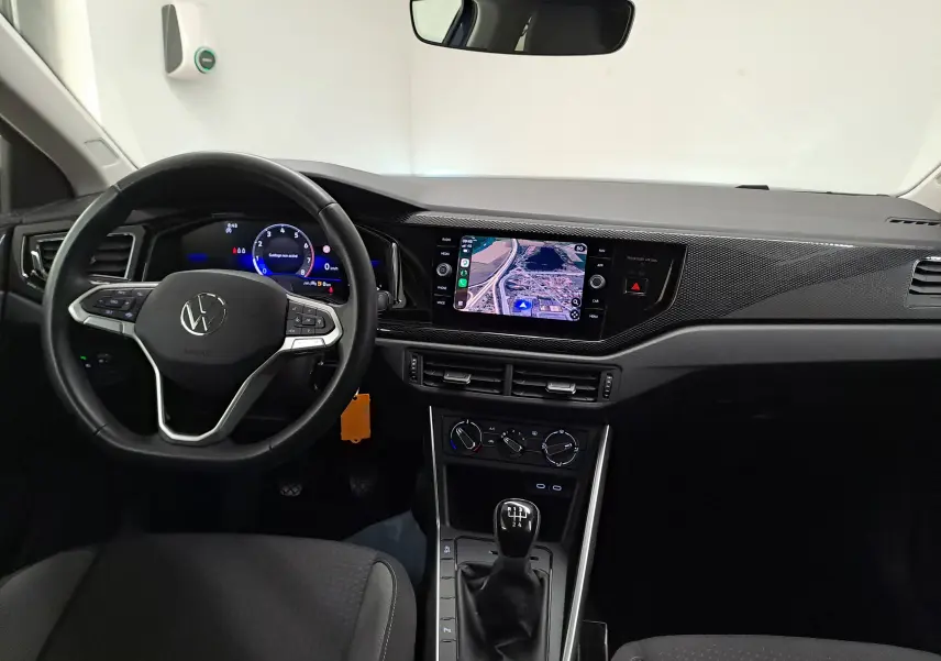 Vue intérieure avant du tableau de bord et volant cuir noir d'une Volkswagen Polo 2025 avec écran tactile et levier de vitesses manuel.