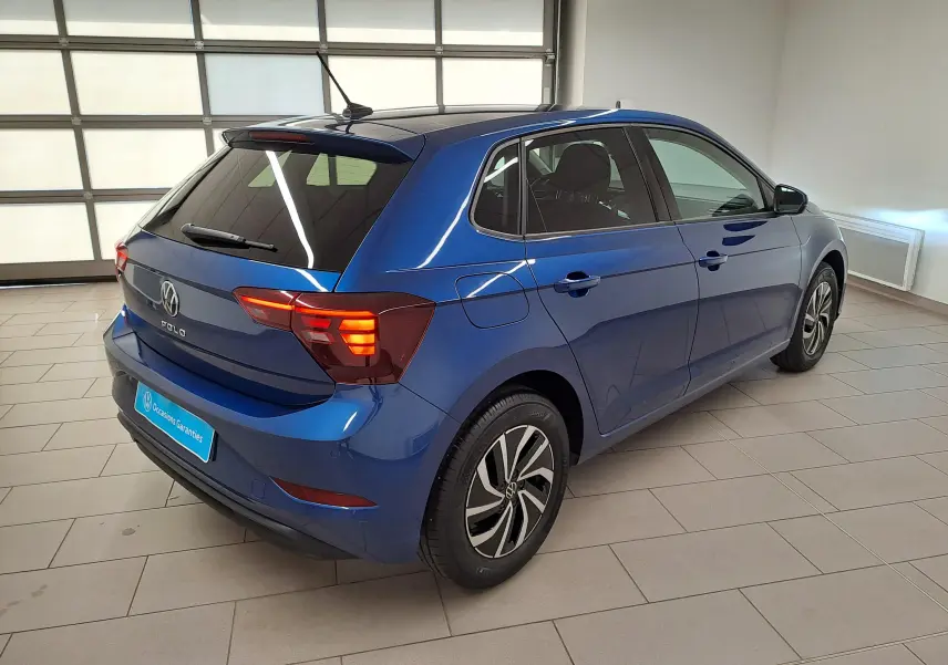 Vue 3/4 arrière droite d'une Volkswagen Polo 2025 bleu récif avec jantes alliage 15'' et vitres surteintées en intérieur showroom.