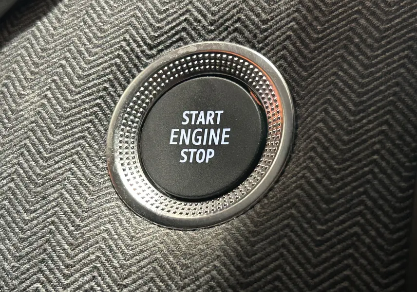 Bouton Start Engine Stop en gros plan sur la console intérieure au tissu gris à motif chevron de la Renault Clio V hybride.
