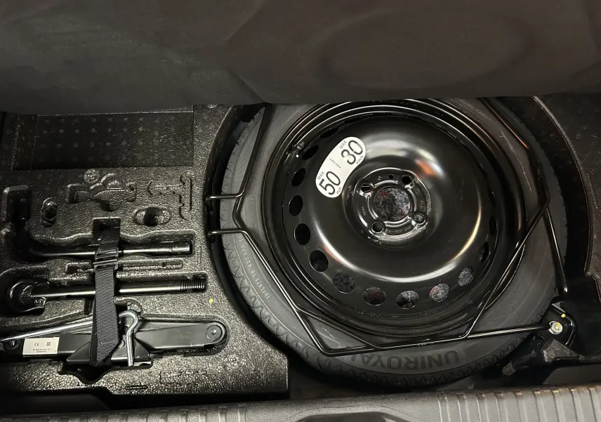 Vue rapprochée de la roue de secours noire et des outils de bord dans le coffre d'une Renault Clio V gris Rafale Métal.
