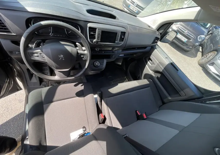 Vue intérieure du poste de conduite du Peugeot Expert Fourgon gris, avec volant multifonctions et banquette bi-ton noir/gris.
