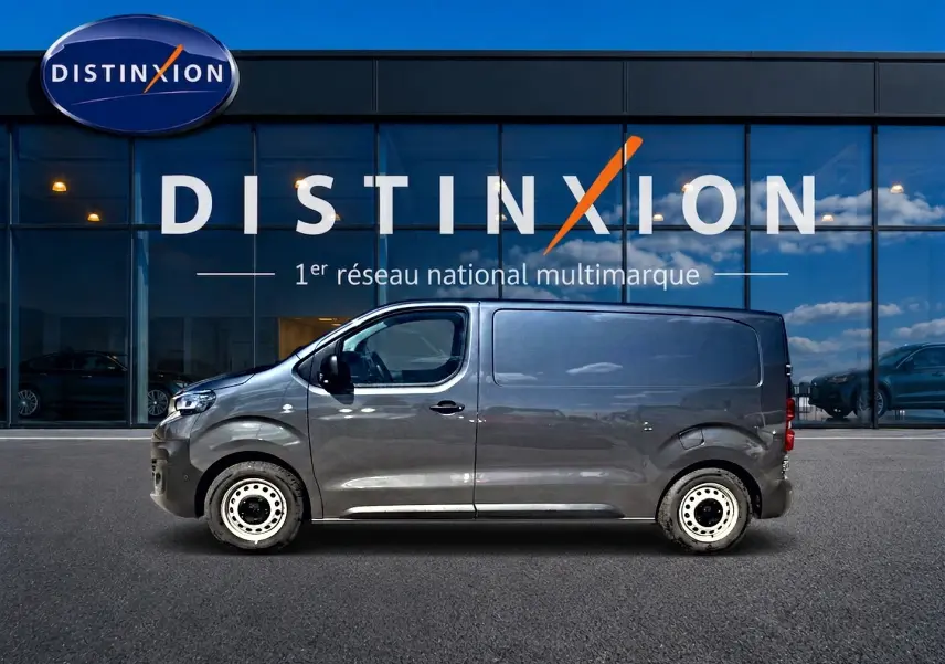 Vue latérale droite d'un Peugeot Expert Fourgon gris 2024 avec porte latérale coulissante, devant une vitrine Distinxion.