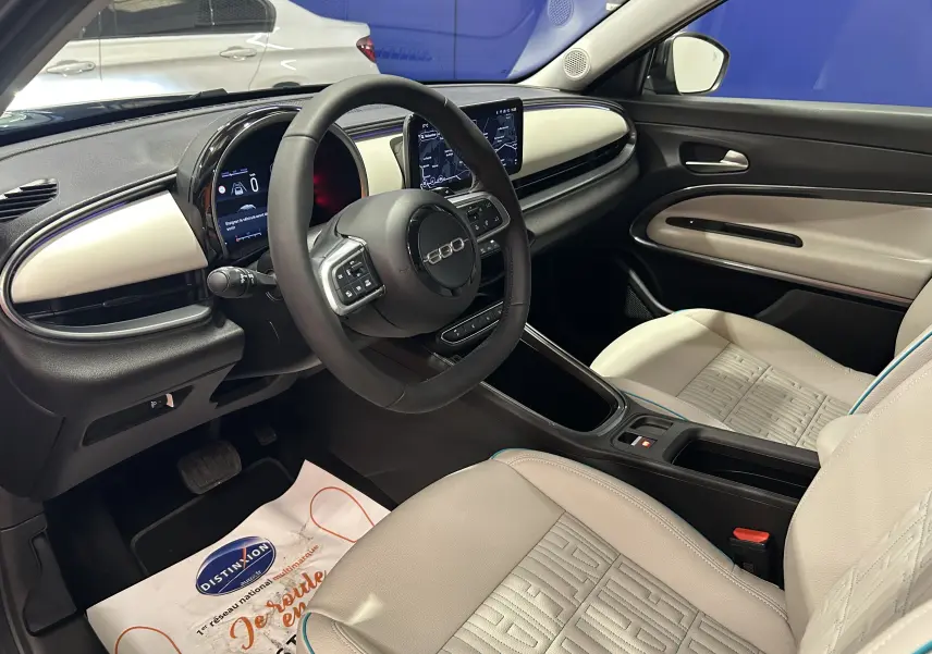 Intérieur clair de la Fiat 600 Hybrid 2024 vu côté conducteur, avec tableau de bord moderne et sièges cuir chauffants.