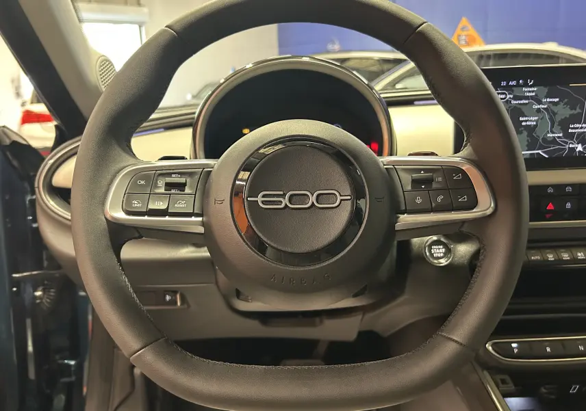Vue rapprochée du volant noir du Fiat 600 Hybrid 2024 avec commandes intégrées et tableau de bord numérique.