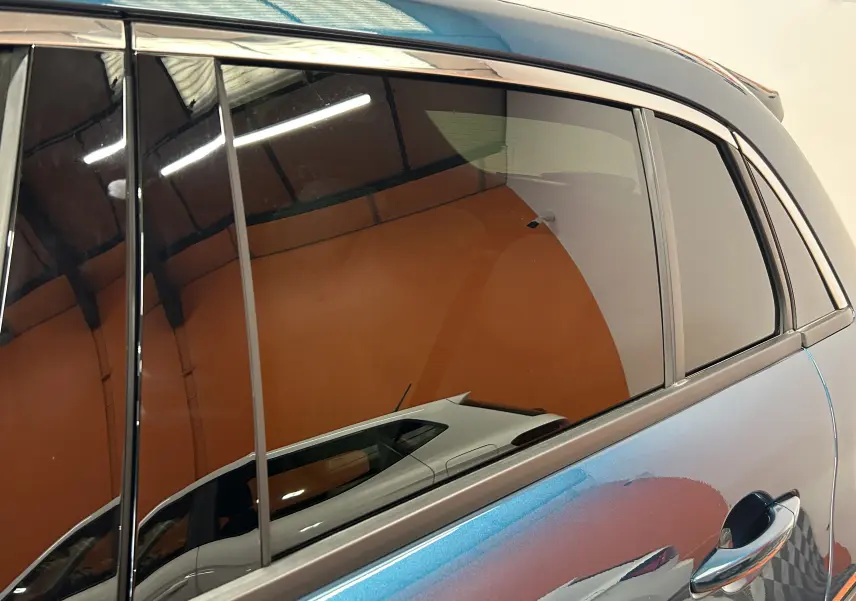 Gros plan sur la porte arrière droite bleu métallisé d'une FIAT 600 Hybrid 2024, avec reflet d'un autre véhicule blanc.