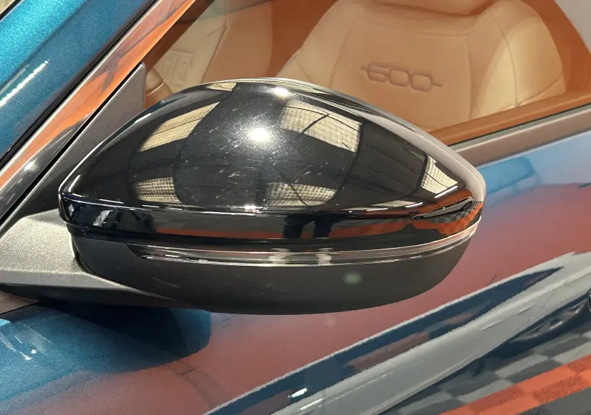 Rétroviseur noir côté gauche d'une FIAT 600 Hybrid 100 La Prima bleu avec intérieur cuir marron visible en arrière-plan.