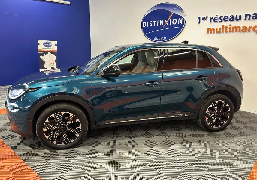 Vue latérale droite d'un FIAT 600 Hybrid 100 La Prima bleu métallisé avec jantes bi-ton et intérieur cuir beige visible.