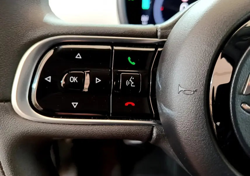 Gros plan sur les commandes gauche du volant cuir noir de la Fiat 500 électrique blanche 2022 Icône.