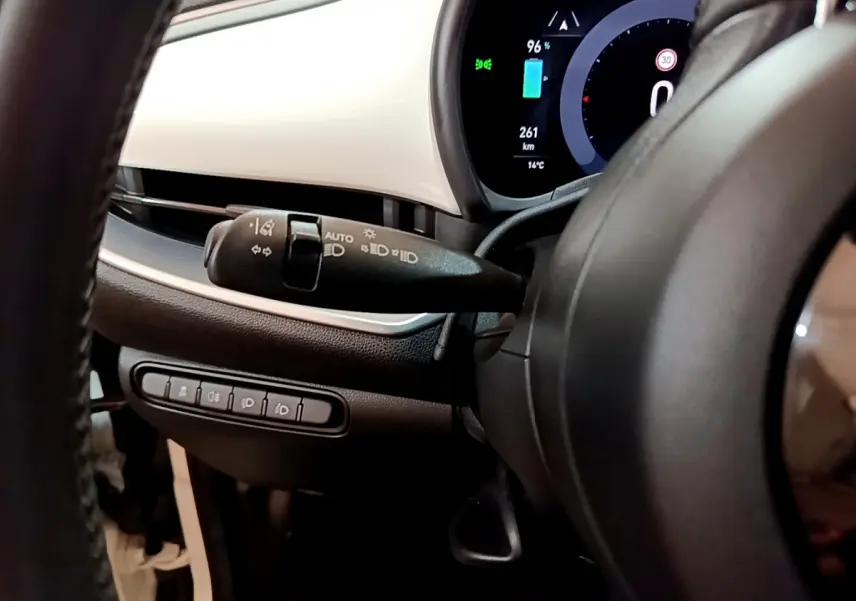 Gros plan sur le combiné d'instruments numérique et la commande des phares à gauche du volant d'une Fiat 500 blanche électrique 2022.