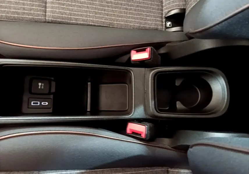Gros plan sur la console centrale noire de la Fiat 500 électrique blanche, avec porte-gobelet et prises USB visibles entre les sièges.