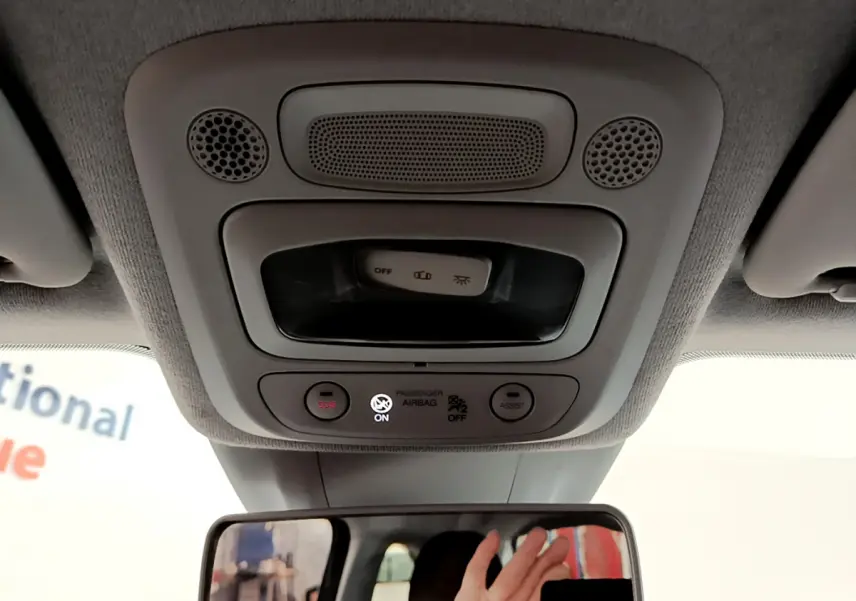 Vue intérieure du plafonnier gris clair avec commandes SOS et assist, rétroviseur et main visible dans une Fiat 500 blanche électrique.