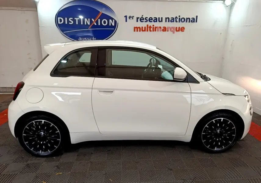 Profil droit d'une FIAT 500 électrique blanche 42kWh Icône 2022 avec jantes noires en intérieur showroom.