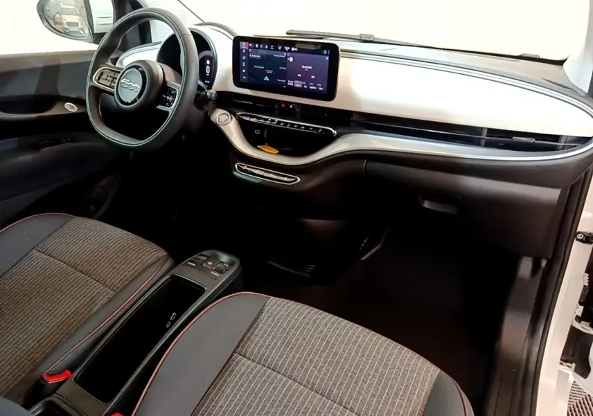 Intérieur avant de la Fiat 500 électrique blanche, tableau de bord moderne avec écran tactile central et sièges gris à surpiqûres rouges.