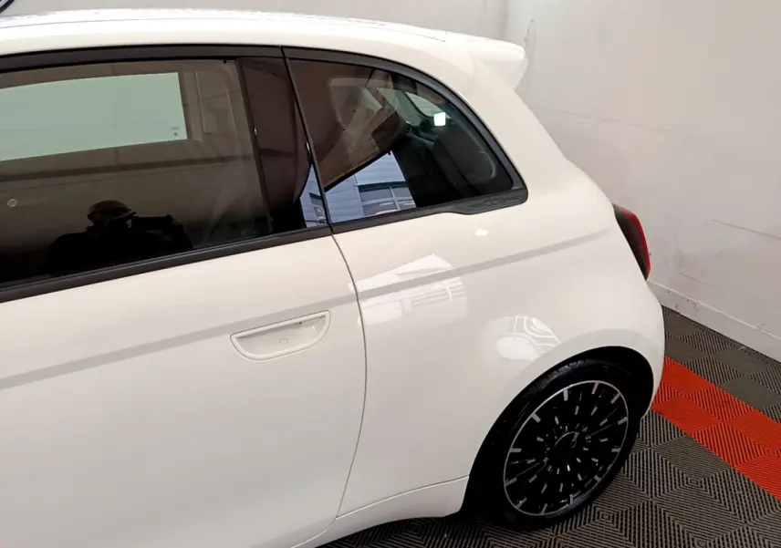 Vue latérale droite rapprochée d'une FIAT 500 électrique blanche avec jante noire et poignée de porte intégrée.