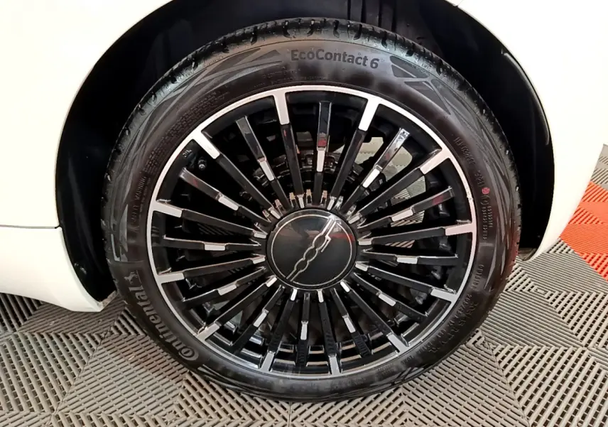 Gros plan sur la roue avant gauche de la FIAT 500 électrique blanche, mettant en valeur la jante noire à rayons fins.