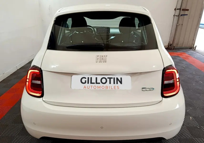 Vue arrière d'une Fiat 500 électrique blanche avec feux LED allumés dans un garage fermé.