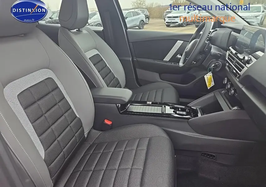 Intérieur avant de la Citroën C4 hybride 2025, vue côté droit, sièges tissu noir et gris avec console centrale brillante.