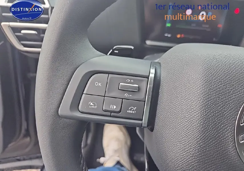 Gros plan sur les commandes gauche du volant en cuir du Citroën C4 bleu eclipse 2025, avec tableau de bord numérique en arrière-plan.