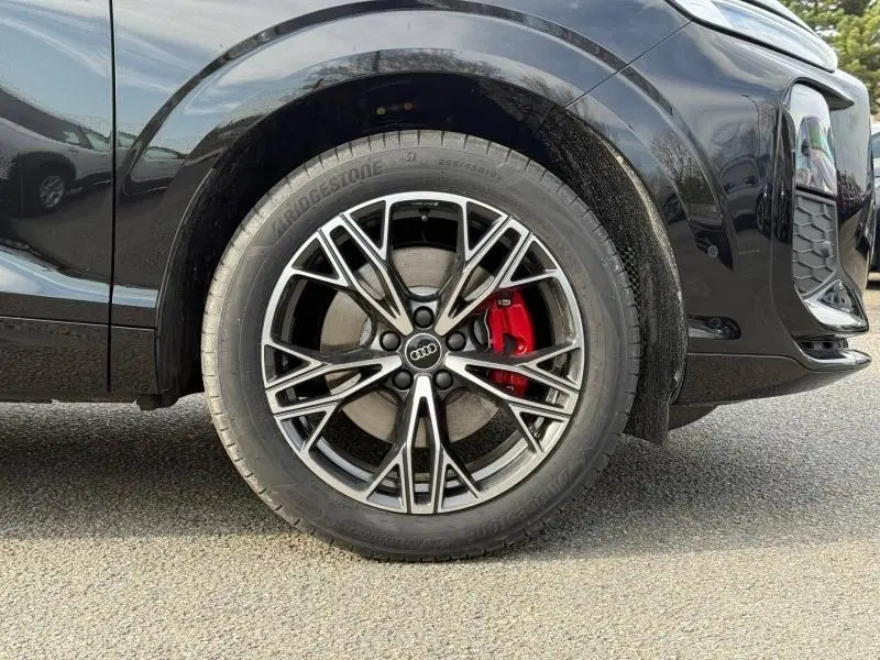 Gros plan sur la roue avant gauche d’un Audi Q3 noir métallisé, avec jante alliage et étrier de frein rouge visible.