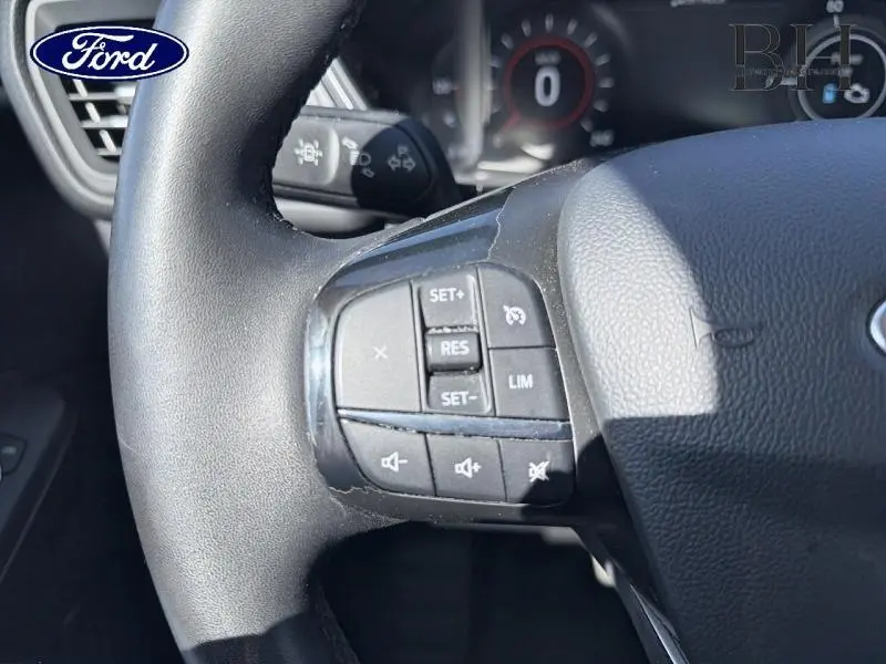 Gros plan sur le volant cuir noir du Ford Kuga 2023, avec commandes multifonctions visibles à gauche.