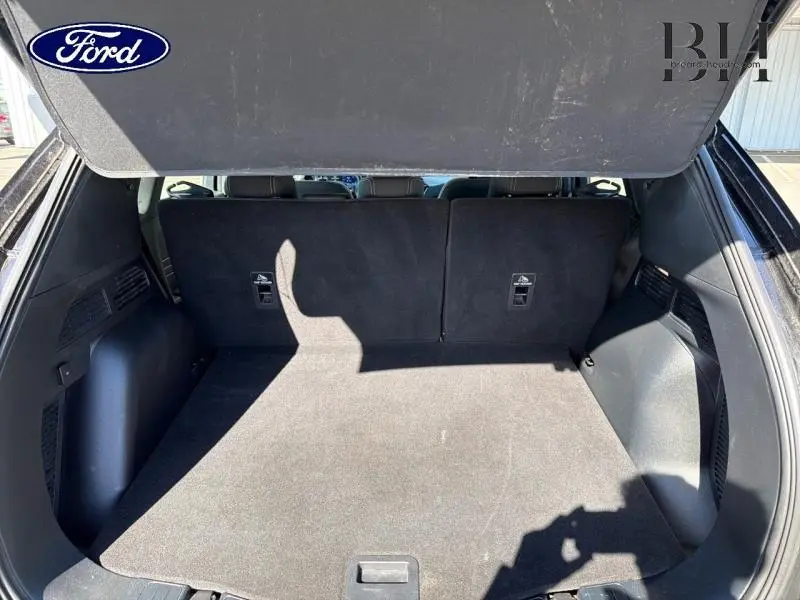 Coffre ouvert vu de l'arrière d'un Ford Kuga noir Agate Métallisée avec banquette arrière relevée et espace de chargement vide.