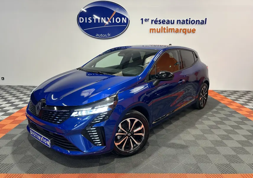 Renault Clio V E-Tech hybride bleu Iron Metal, vue 3/4 avant droit avec phares LED allumés en showroom.