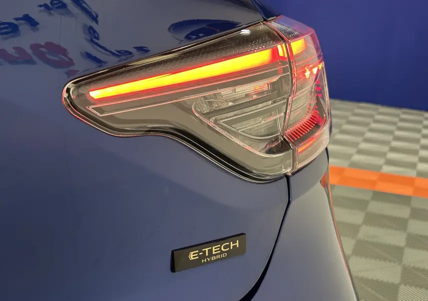 Gros plan sur le feu arrière droit allumé d’une Renault Clio V bleu Iron Metal avec badge E-TECH Hybrid visible.