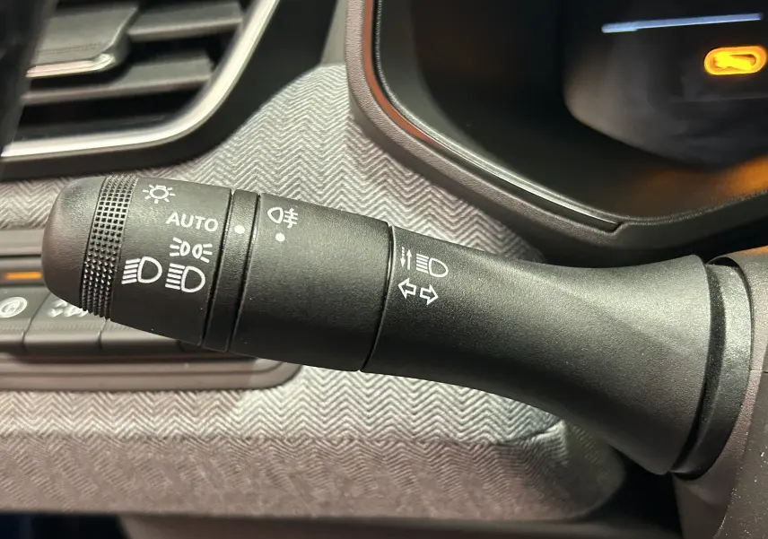 Gros plan sur la commande de phares et clignotants noire dans l’habitacle gris de la Renault Clio V hybride 2025.