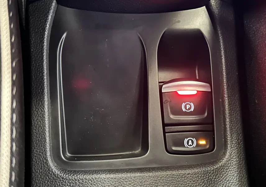 Gros plan sur la console centrale de la Renault Clio V hybride, avec bouton de frein à main électronique et indicateur lumineux.