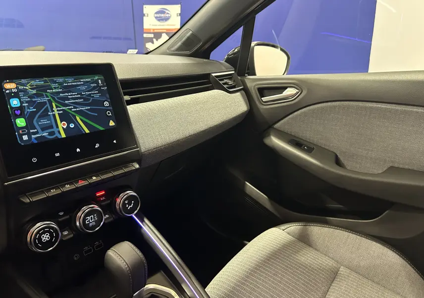 Vue intérieure côté passager de la Renault Clio V E-Tech avec tableau de bord gris et écran tactile affichant la navigation.