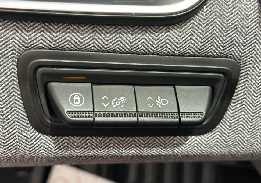 Gros plan sur les commandes de réglage des feux et verrouillage, sur tissu gris à motif chevrons dans une Renault Clio V bleu Iron Metal.