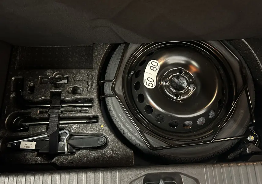 Vue en plongée sur la roue de secours et les outils de bord rangés dans le coffre d'une Renault Clio V bleu Iron Metal.