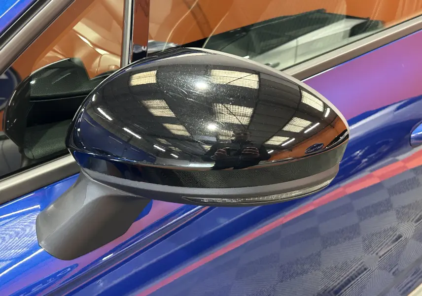 Rétroviseur noir brillant côté gauche d’une Renault Clio V bleu iron metal, avec reflet intérieur visible.