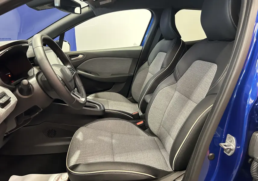 Vue intérieure côté conducteur de la Renault Clio V bleu iron metal, sièges tissu gris et cuir noir avec surpiqûres blanches.