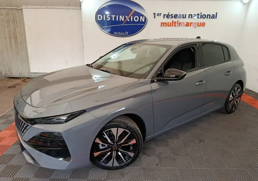 Peugeot 308 gris foncé vue 3/4 avant droit, avec jantes alliage noires et calandre distinctive en intérieur showroom.