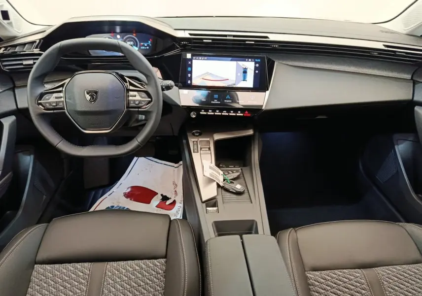 Vue intérieure avant de la Peugeot 308 2026, volant cuir multifonctions, écran tactile central et console gris foncé.