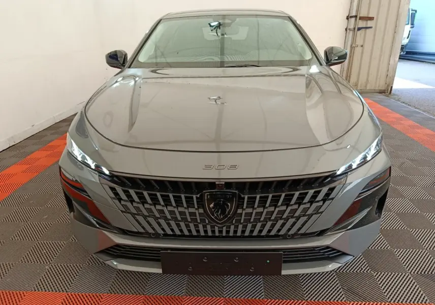 Vue avant d'une Peugeot 308 gris foncé avec calandre distinctive et phares LED fins dans un garage.