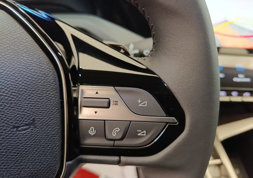 Gros plan sur les commandes du volant cuir gris de la Peugeot 308 BlueHDi 130, avec écran tactile en arrière-plan.