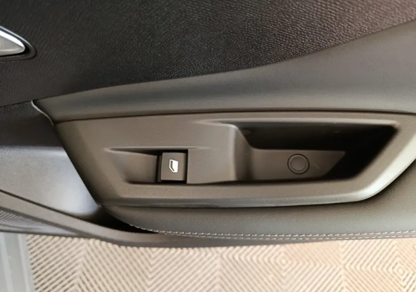 Gros plan sur la poignée intérieure de porte côté gauche d'une Peugeot 308 gris foncé, avec bouton de commande de vitre.