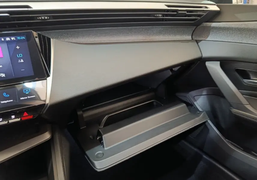 Intérieur Peugeot 308 BlueHDi 2026, vue côté passager sur boîte à gants ouverte et tableau de bord noir.