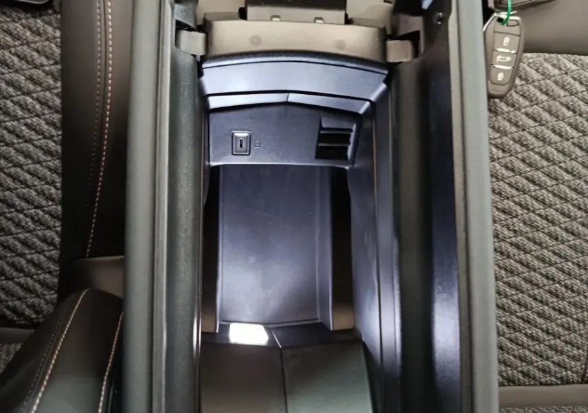 Vue plongeante sur l'accoudoir central ouvert de la Peugeot 308 gris foncé, avec prise USB visible et clé de voiture posée.