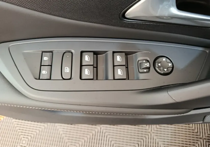 Gros plan sur les commandes de lève-vitres et rétroviseurs sur la porte côté conducteur d’une Peugeot 308 gris foncé.