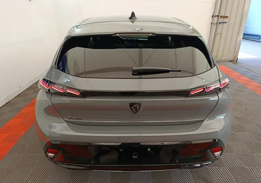 Vue arrière d'une Peugeot 308 gris foncé 2026 avec feux LED et lunette arrière teintée dans un garage.