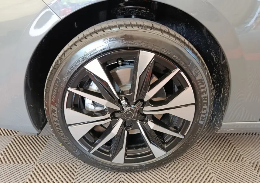 Gros plan sur la roue avant droite d'une Peugeot 308 gris foncé avec jante alliage bicolore et logo central Peugeot.