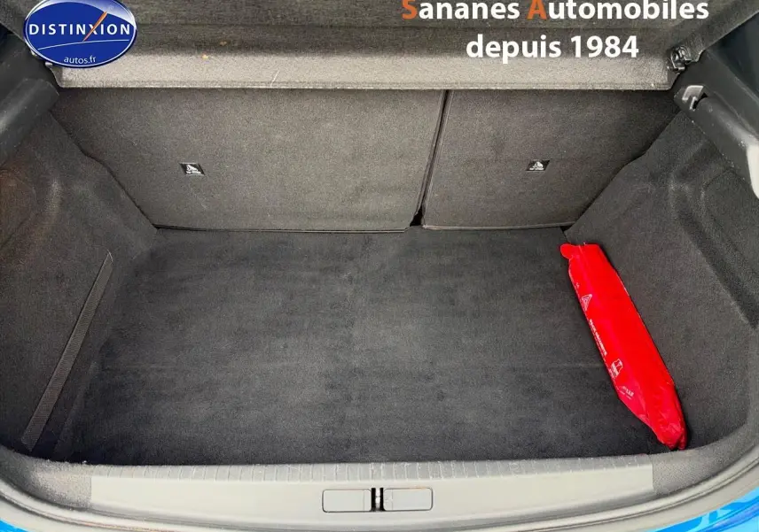 Coffre ouvert d'une Peugeot 208 GT Line bleu clair, montrant un espace de rangement propre avec un triangle de signalisation rouge.