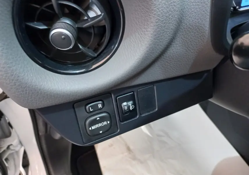 Gros plan sur commandes de réglage des rétroviseurs et ventilation côté conducteur de Toyota Yaris blanche 2019.