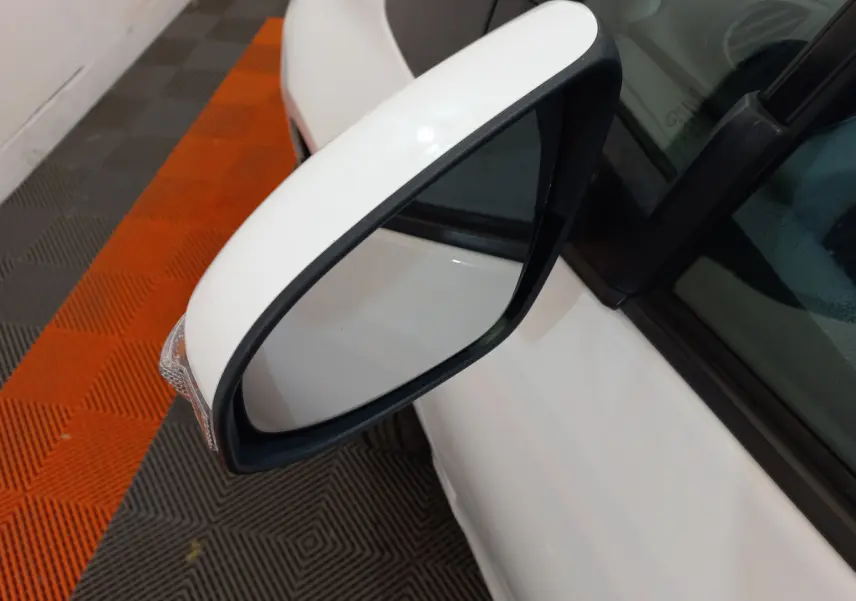 Rétroviseur côté gauche blanc de la Toyota Yaris hybride 2019, vue rapprochée sur fond de sol orange et gris.