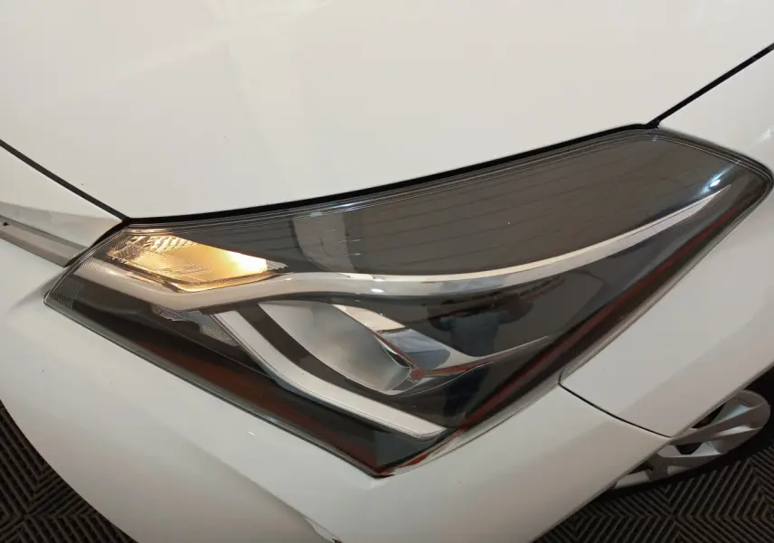 Gros plan sur le phare avant gauche allumé d'une Toyota Yaris blanche 2019, soulignant son design moderne et épuré.