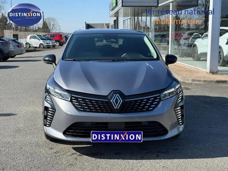 Vue de face d'une Renault Clio gris schiste 2025 avec calandre noire et feux LED distinctifs allumés.